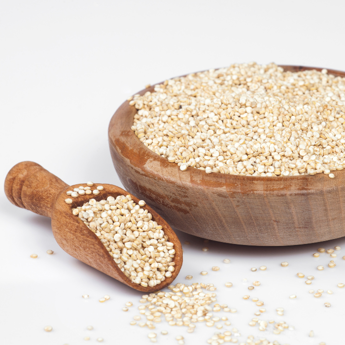 White quinoa in a wooden bowl and scoop on a white background