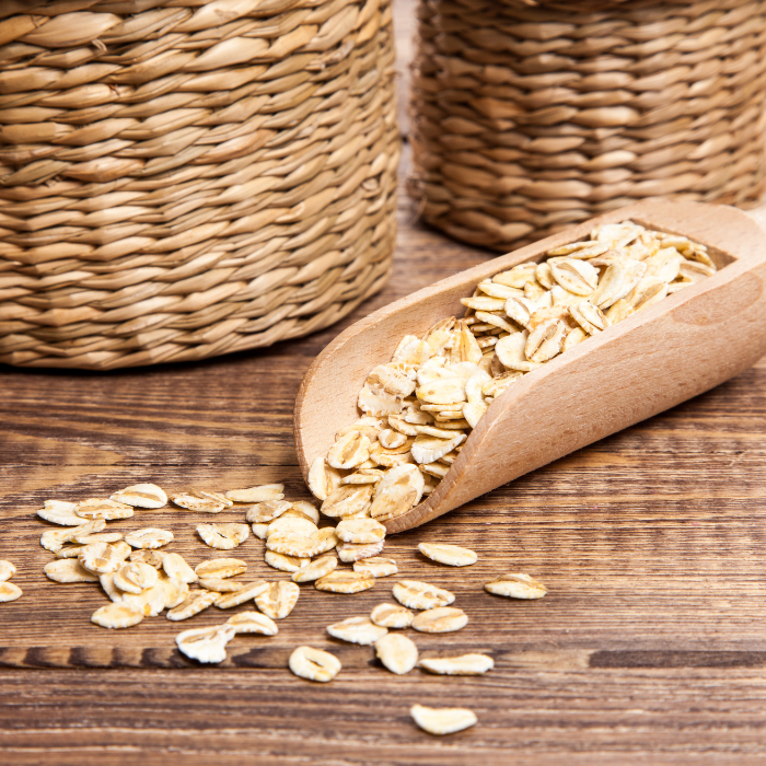 Barley flakes in a wooden spoon next to woven baskets on a wooden surface