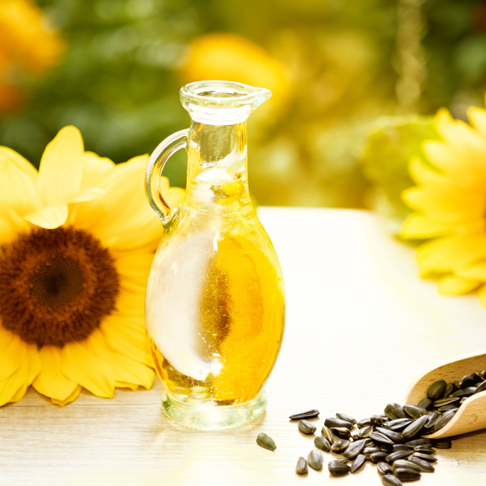 Sunflower oil in a glass bottle next to a scoop of sunflower seeds and sunflowers on a wooden surface