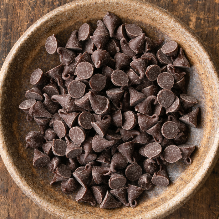 Carob chips in a ceramic bowl on a wooden surface