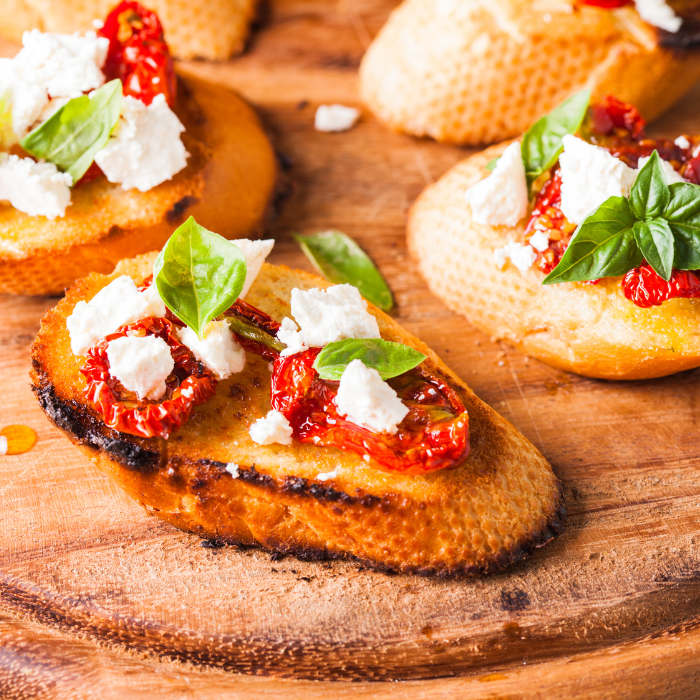 Baguette slices with sundried tomato, cheese, and basil on a wooden board