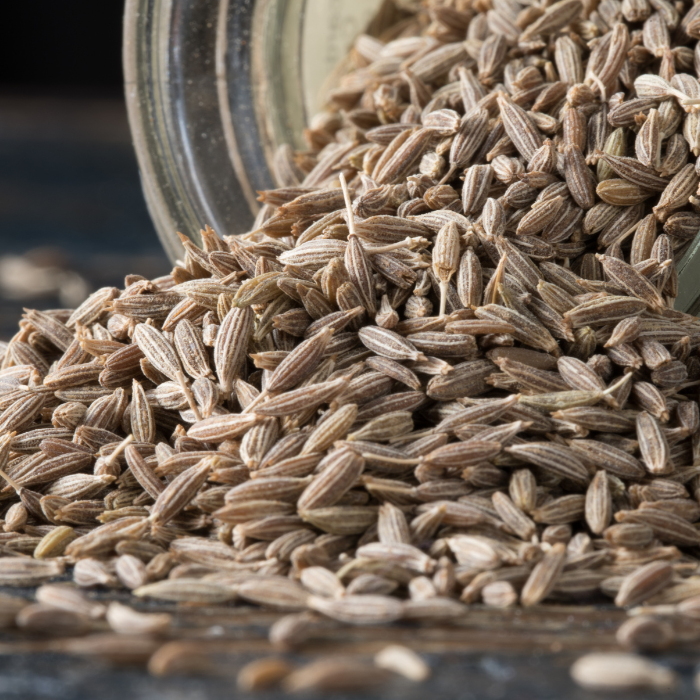 Whole cumin seeds coming out of a clear glass jar