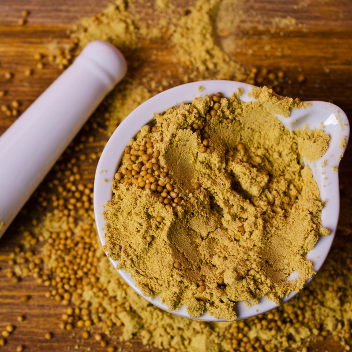 Mustard seed powder and mustard seed in a white mortar and pestle on a wooden background