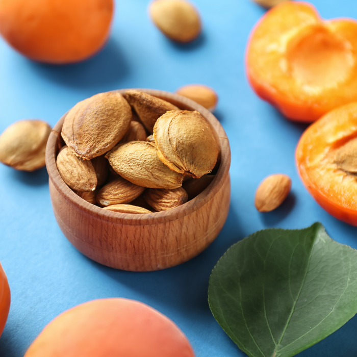 Apricot shells in a wooden bowl next to fresh apricots with a blue background