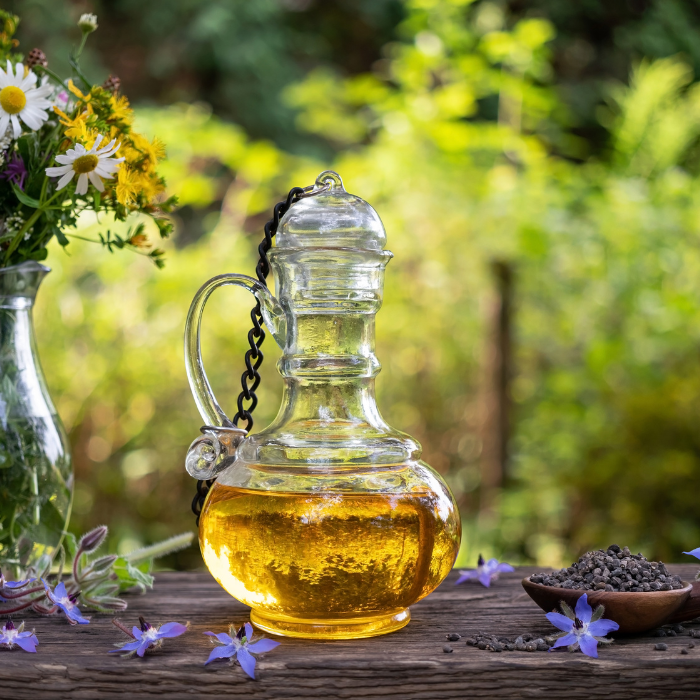 Borage seed oil in a clear glass bottle next to a wooden bowl of borage seed 