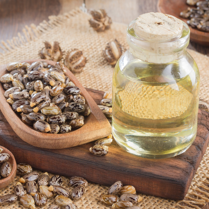 Castor oil in a glass bottle next to castor beans on a wooden board