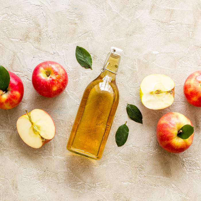 Apple cider vinegar in a clear glass bottle arranged next to apples and leaves on a beige background