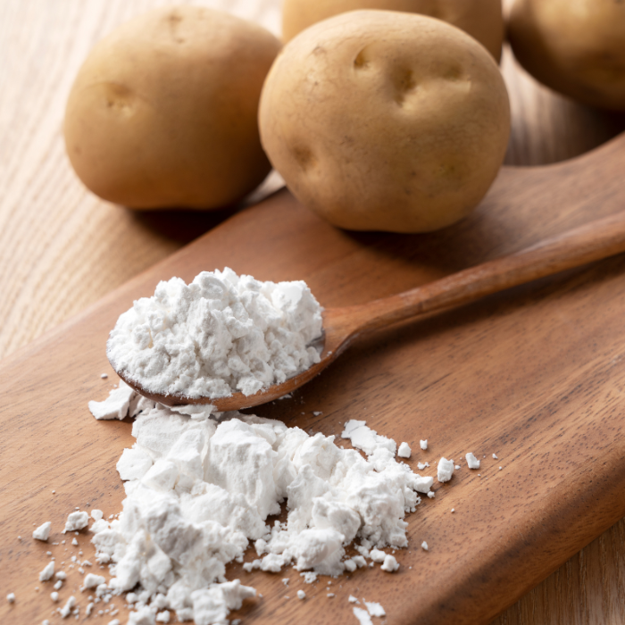 Potato starch on a wooden cutting board with a wooden spoon next to potatoes