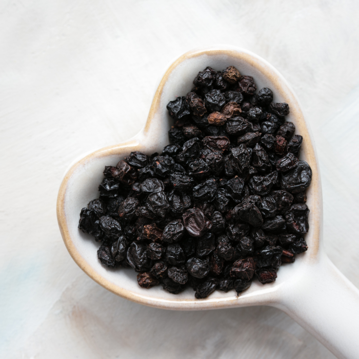 Elderberries in a ceramic white heart-shaped spoon with a white background