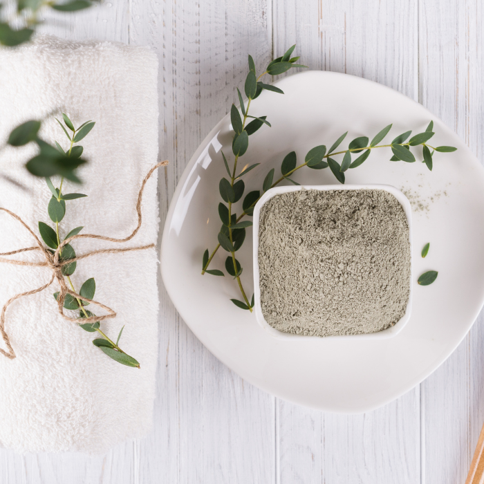 Bentonite clay in a white bowl on a white plate with leaves 