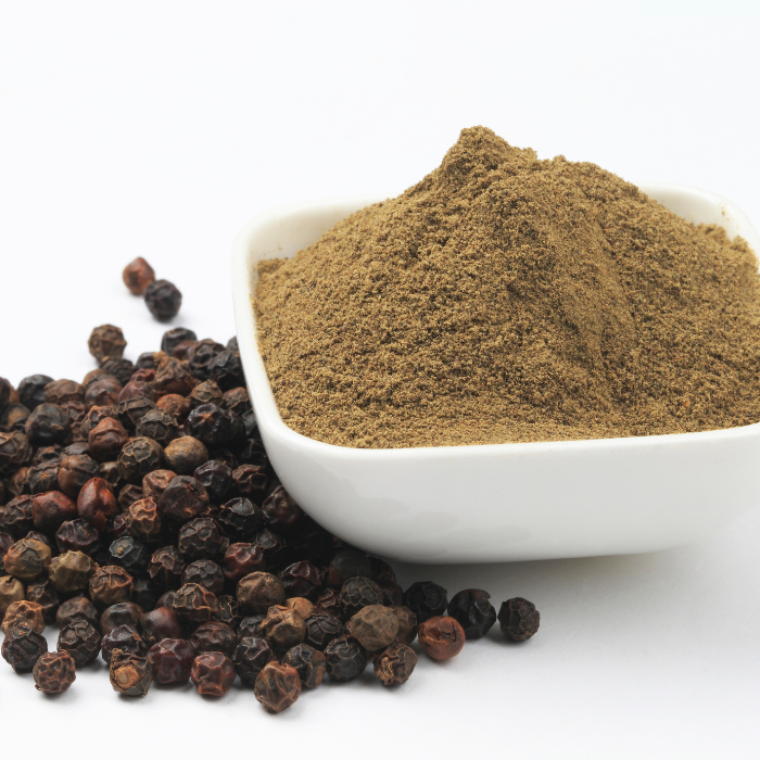 Fine grind black pepper in a white bowl next to whole peppercorns with a white background