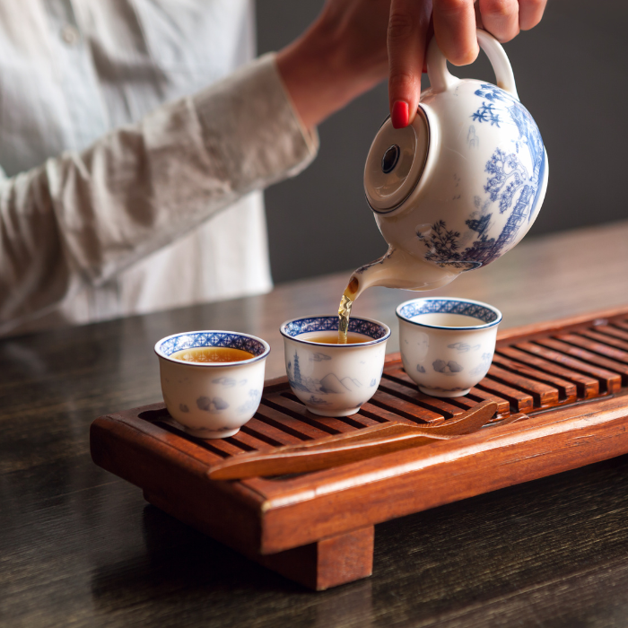 Chinese green tea being poured into blue and white teacups on a wooden stand