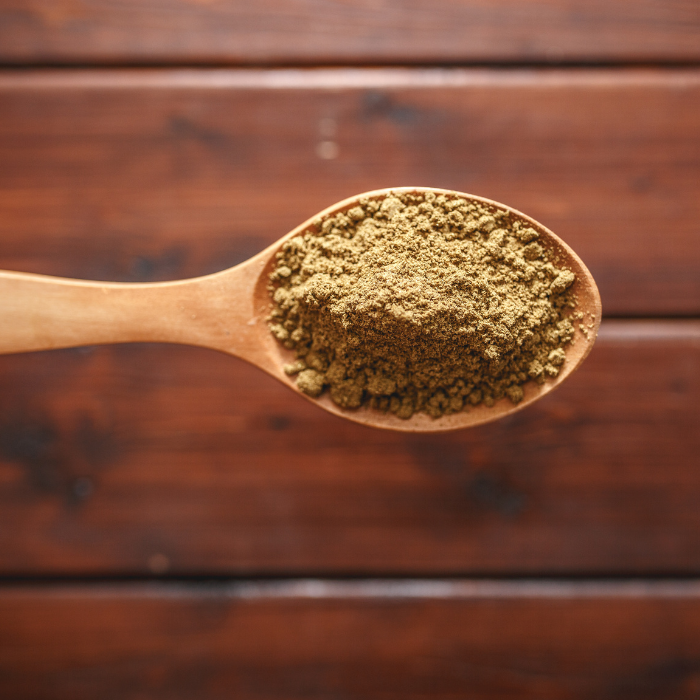 Ground cumin in a wooden spoon above a wooden surface