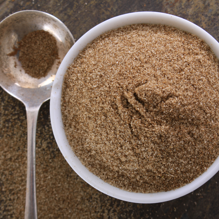 Celery salt in a white bowl next to a metal spoon on a wooden background