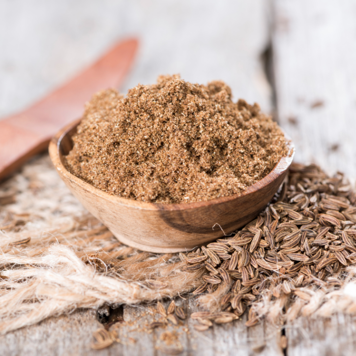 Ground caraway seeds in a wooden bowl next to whole caraway seeds on a wooden background