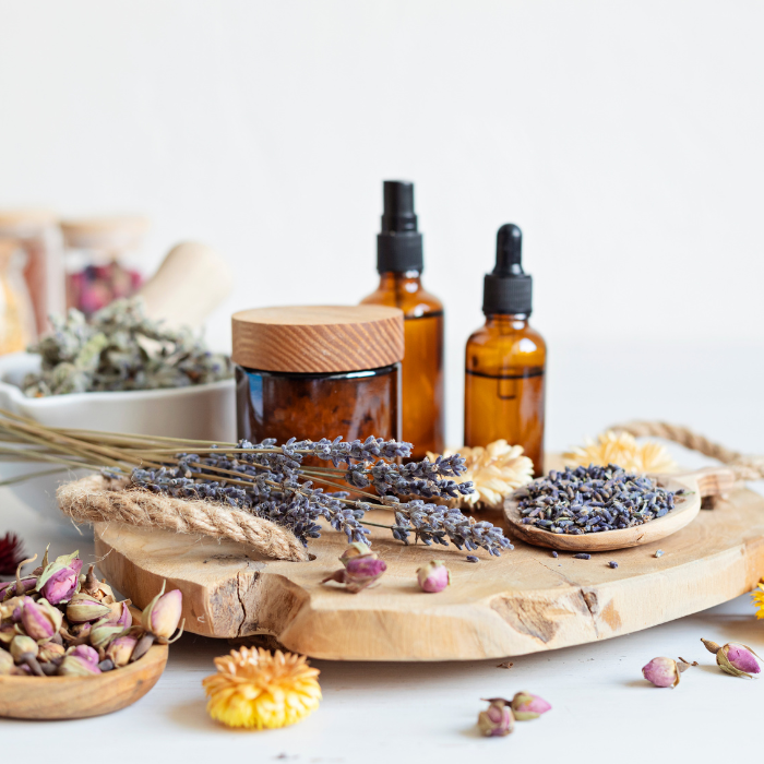 An assortment of bath herbs and oils on a round piece of wood with a white background