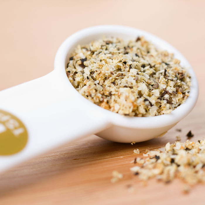 Lemon pepper seasoning in a white 1 tsp measuring spoon on a wooden background