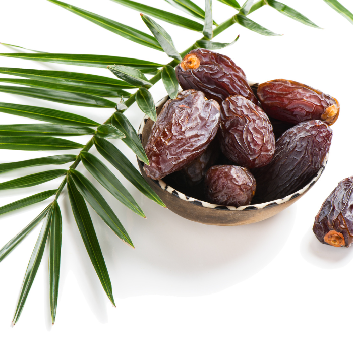 Medjool dates in a decorative bowl next to a leaf on a white background