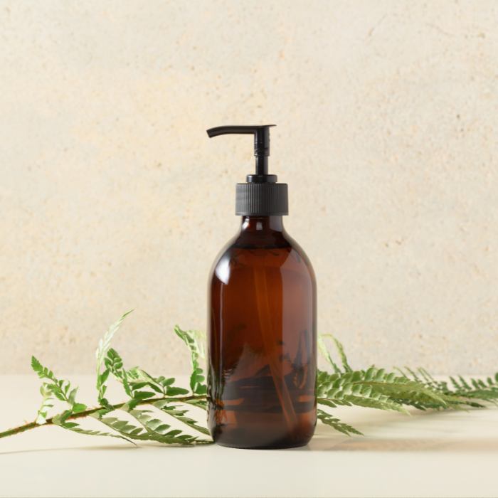 Mild facial cleanser in an amber bottle with a beige background next to a fern leaf