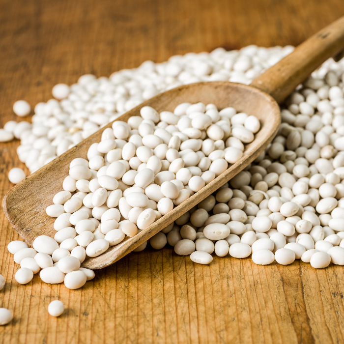 Navy beans on a wooden scoop on a wooden surface