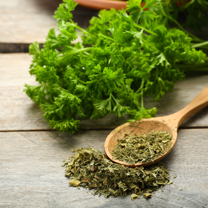 Dried parsley in a wooden spoon next to fresh parsley on a wooden background