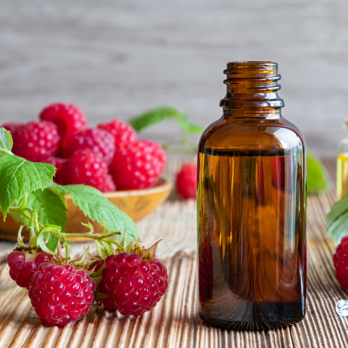 Raspberries next to a bottle of raspberry seed oil on a textured wooden surface