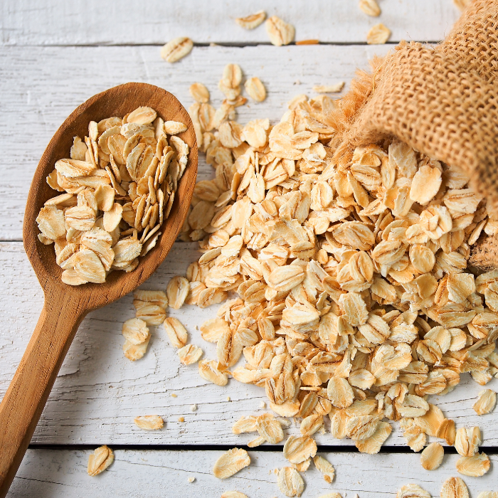 Rolled oats in a wooden spoon and burlap sack on a wooden background