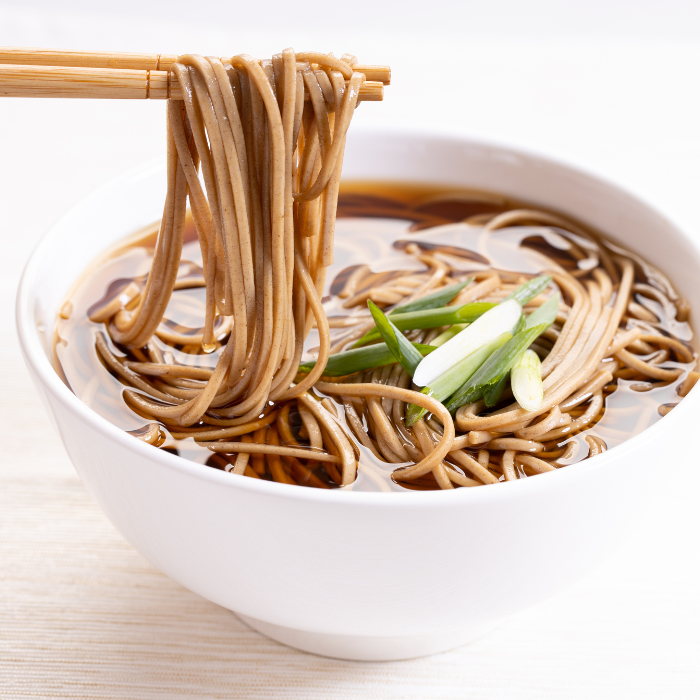 Soba noodles in broth in a white bowl with green onions