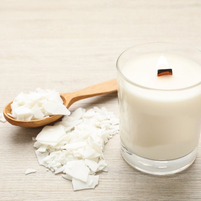 A soy wax candle next to a wooden spoon filled with soy wax