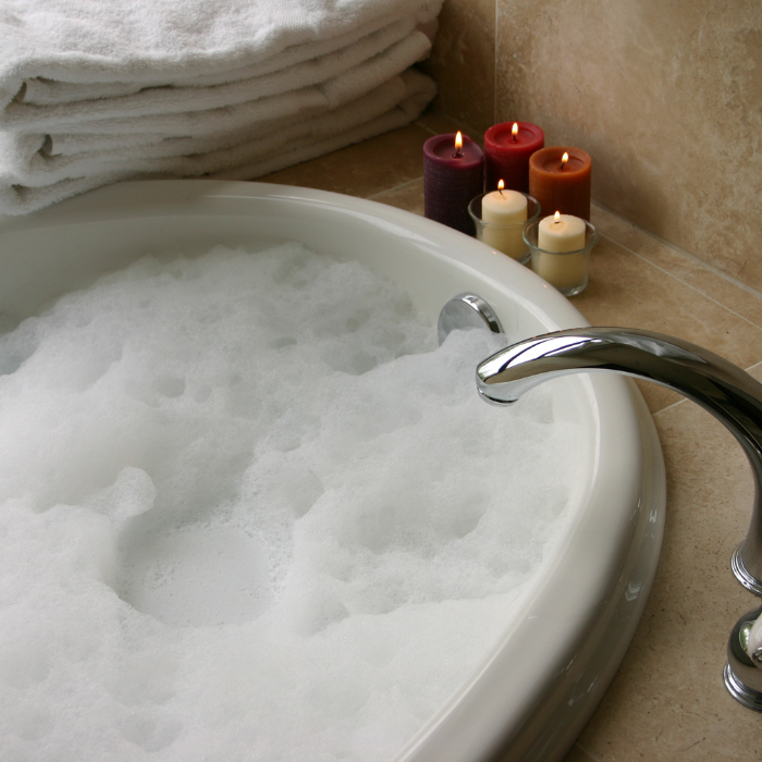 A bathtub filled with bubbles with candles and white towels