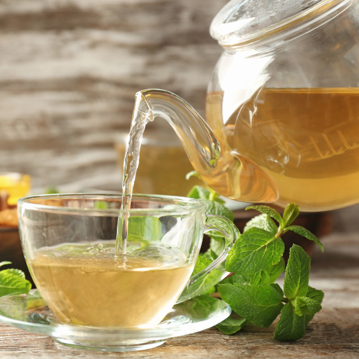 Tea being poured out of a glass teapot into a glass teacup on a wooden surface